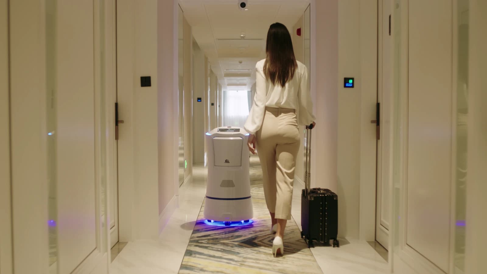 Yomie M6 recorre un pasillo de hotel junto a una huésped.